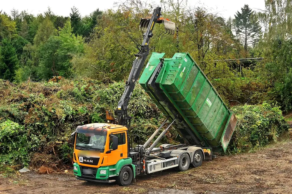 Camion multibenne avec grue déchargeant un container vert